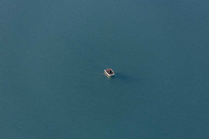 A lone fisherman in a small boat on a vast blue lake