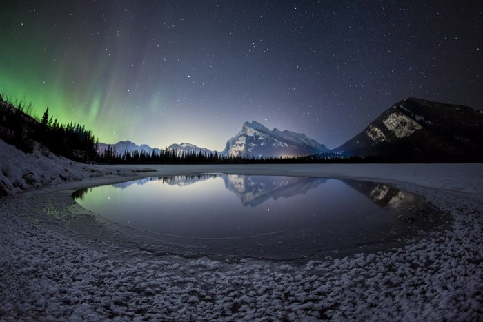 Aurora Borealis over frozen lake and mountains at night