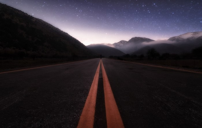 Person on a road at night with mountains and stars