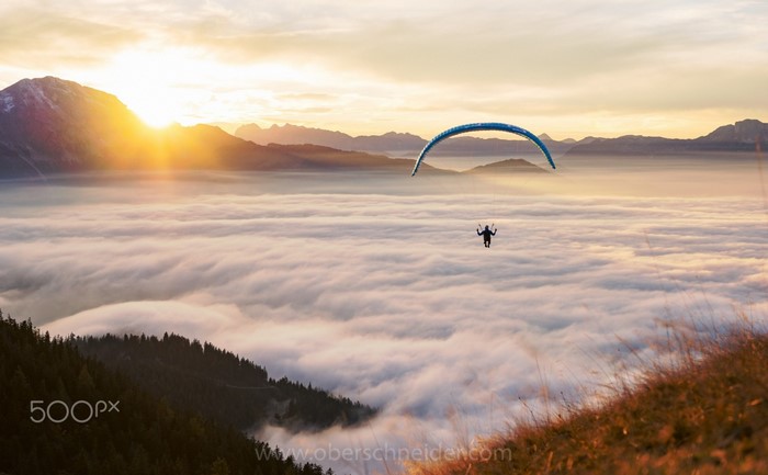 Paraglider flying over clouds at sunrise with mountains