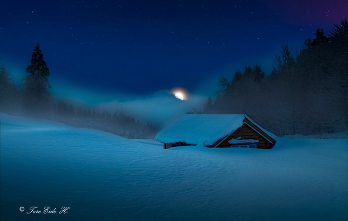 Snow covered cabin at night with moon and stars