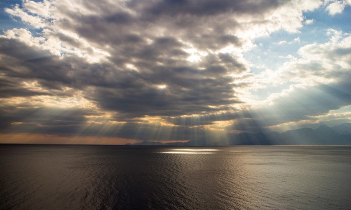 Sunbeams breaking through clouds over the sea at sunset