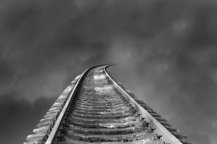 Railroad tracks curving into dark, cloudy sky