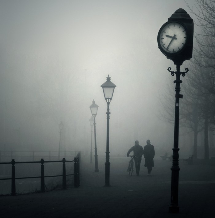 Two people walk past streetlights in the fog