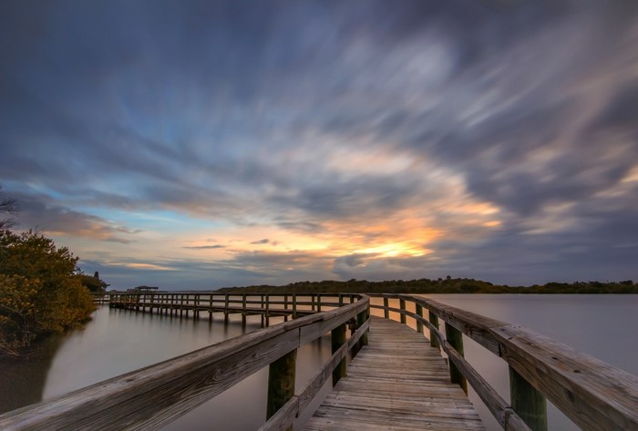 Wooden pier over calm water at sunset with dramatic clouds