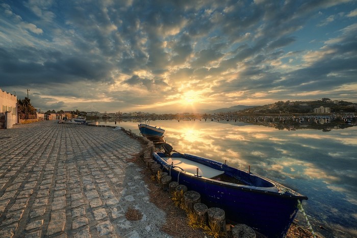 Boats docked by a cobblestone path at sunset with reflections
