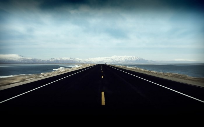 Empty highway by the sea with snow-capped mountains