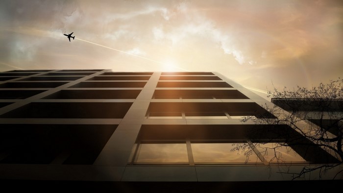 Airplane flying over modern building at sunset