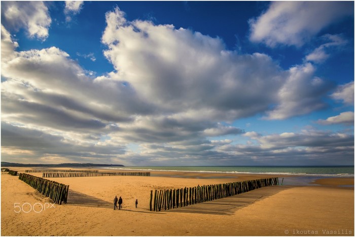 Wooden groynes on a sandy beach under a cloudy sky