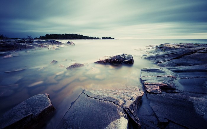Long exposure of rocky shore with calm water and cloudy sky