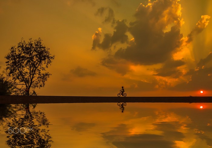 Silhouette of a child on a bicycle at sunset reflected in water