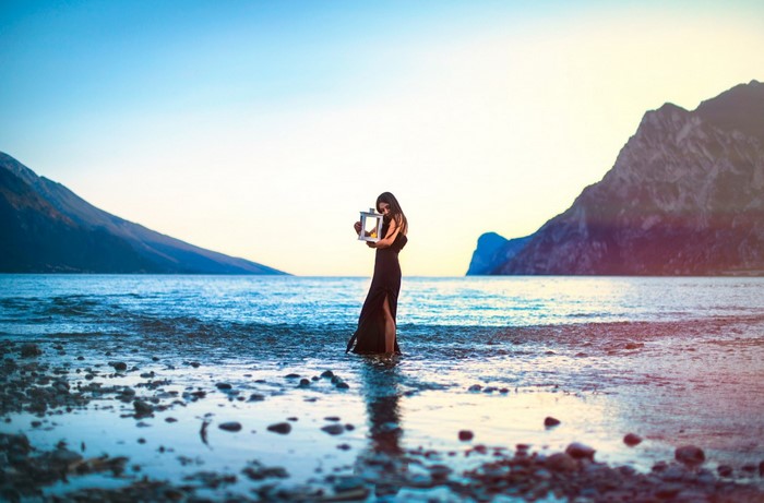 Woman in black dress holding a lantern by the sea