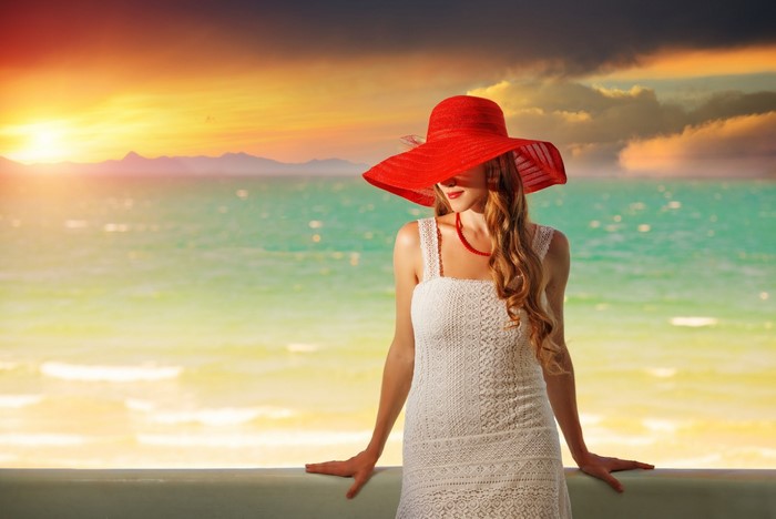 Woman in red hat and white dress at sunset by the sea