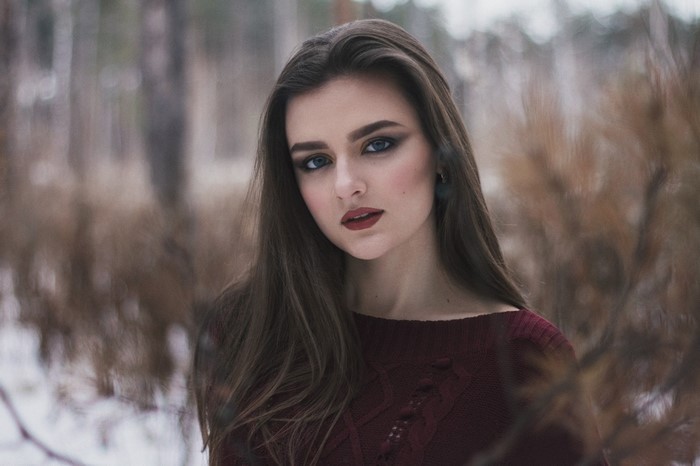 Woman with dark makeup in a maroon sweater outdoors