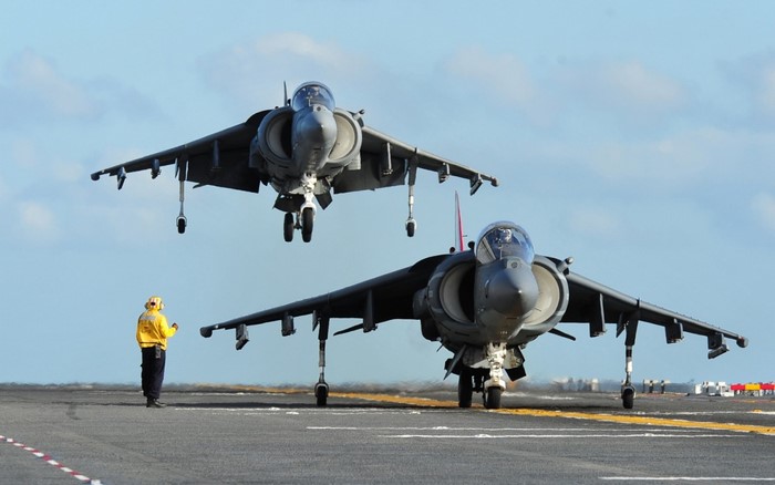 Two AV-8B Harrier II jets on a carrier deck with a crew member
