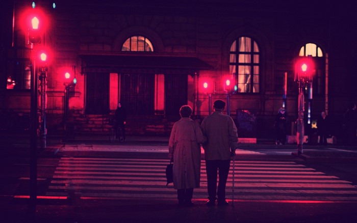 Elderly couple crossing street at night under red lights