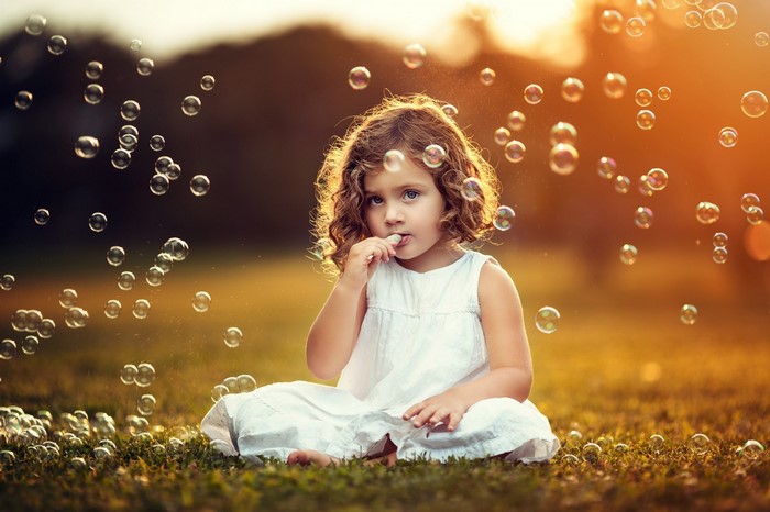 Young girl blowing bubbles in a field at sunset