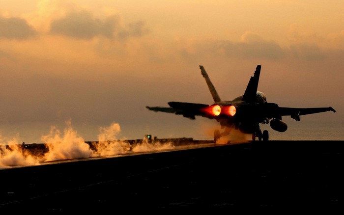 F/A-18 Hornet taking off from aircraft carrier at sunset