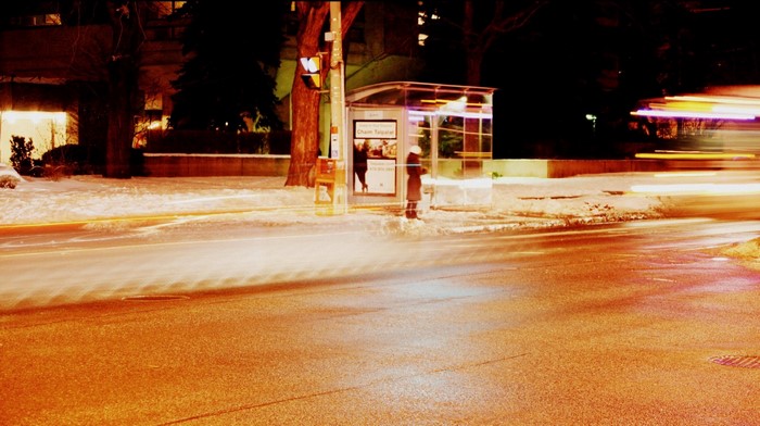 Nighttime bus stop with light trails on a snowy street