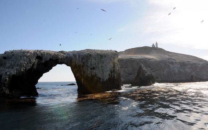 Natural arch rock formation with lighthouse on island