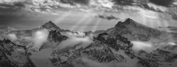 Monochrome panorama of sunbeams over snowy Alps mountain range