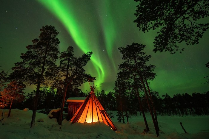 Tipi lit by fire under Aurora Borealis