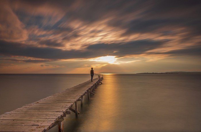 Person on a pier at sunset over the sea