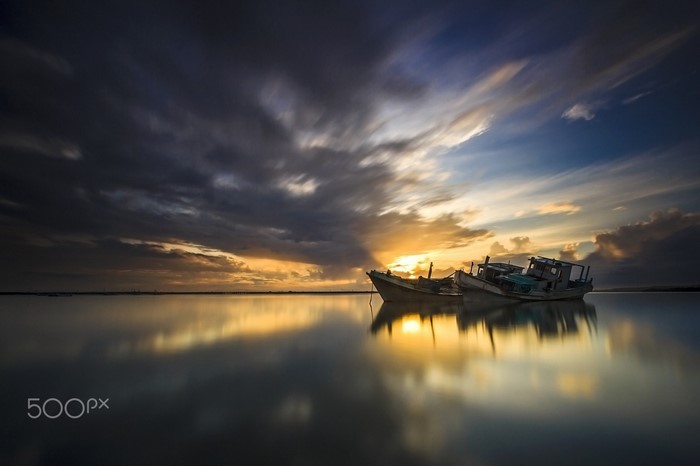 Sunlight reflecting on sea with boats at sunset