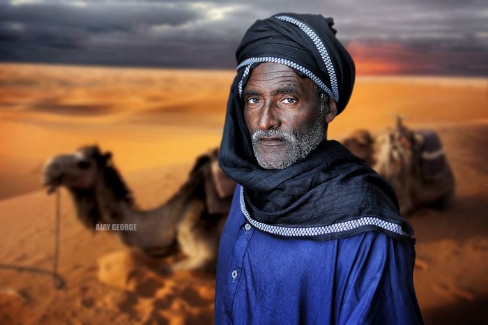 Man in turban and blue robe with camels in desert