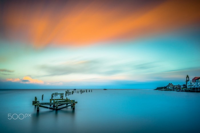 Sunset over the sea with old pier and coastal town