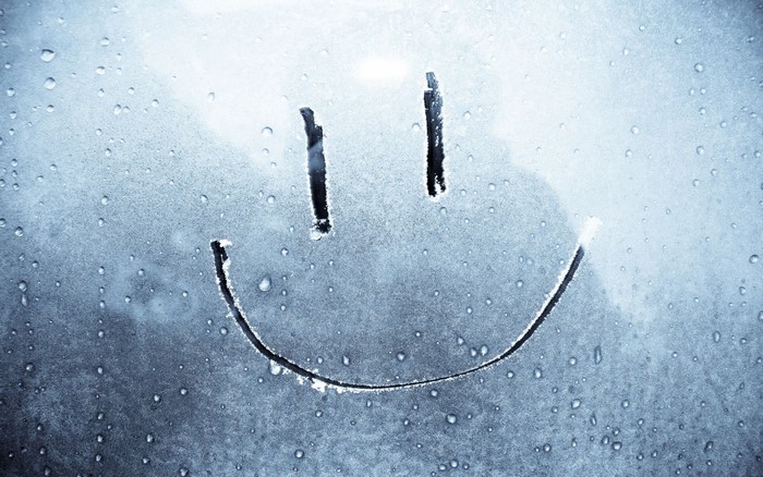 Smiley face drawn on a foggy window with water droplets