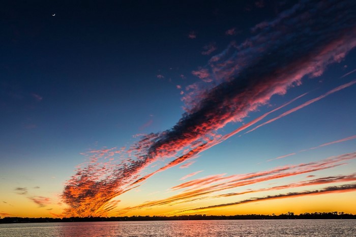 Sunset over water with colorful clouds and moon