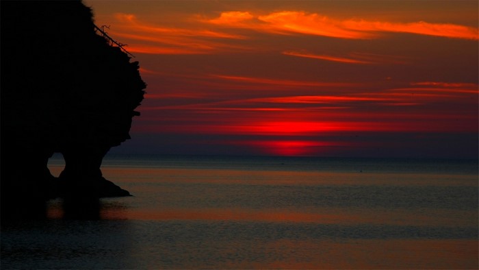 Silhouette of a rock formation against a vibrant sunset over the ocean