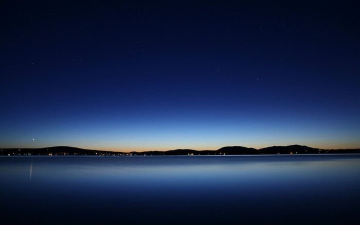 Calm lake at dusk with stars in the sky