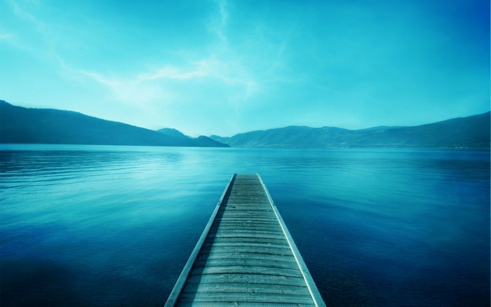 Wooden pier on a calm lake with mountains under a blue sky