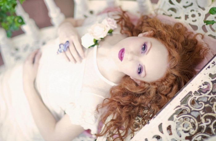 Woman with red curly hair and purple makeup lying down