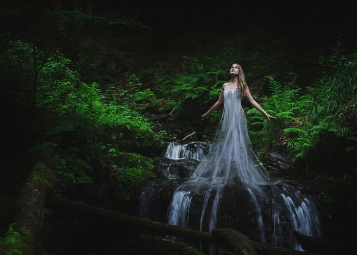 Woman in a flowing dress by a waterfall in a forest