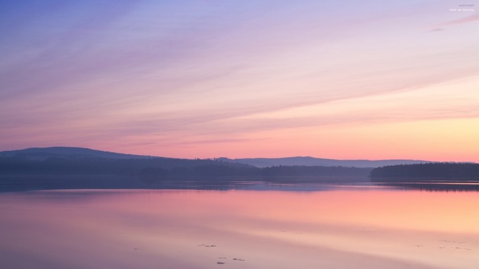 Calm lake reflecting a pastel sunset sky over distant hills