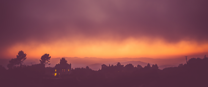 Sunset over mountains with silhouetted trees and house