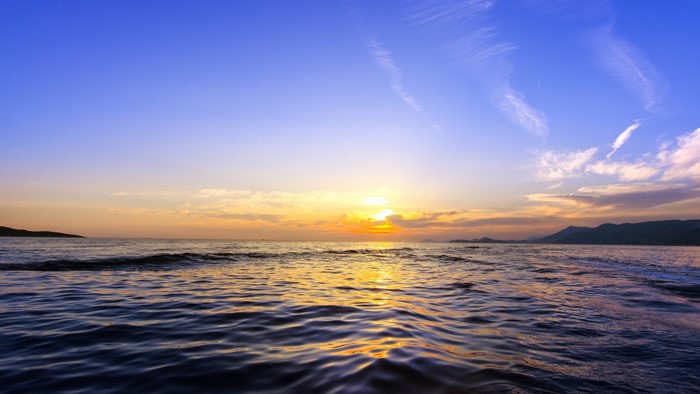 Sunset over the ocean with waves and distant mountains