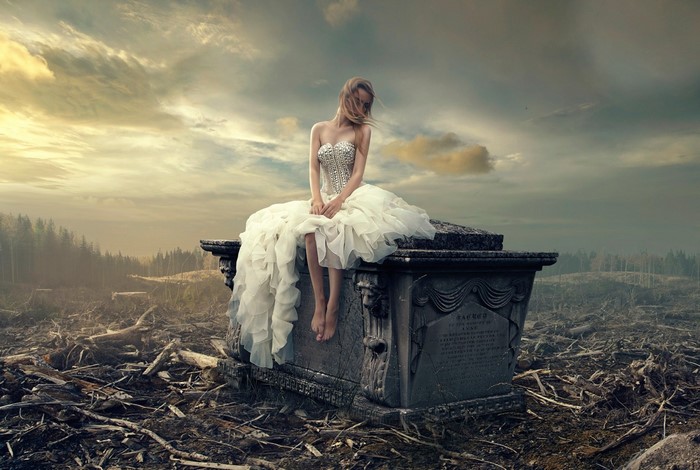 Woman in wedding dress on tombstone in desolate landscape