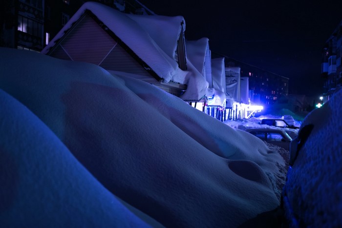 Snow-covered houses and cars at night with blue lights