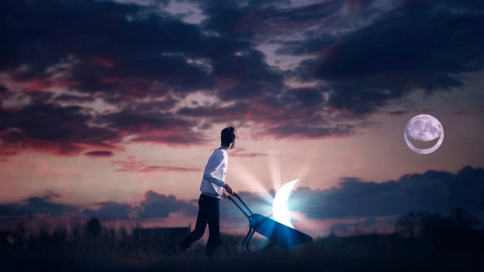 Man pushing wheelbarrow with crescent moon at sunset