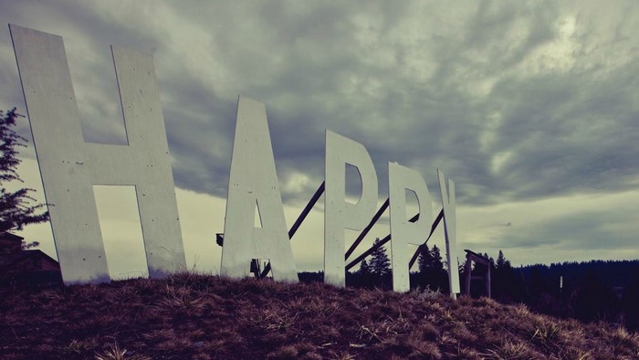 Giant "HAPPY" sign on a grassy hill under cloudy sky
