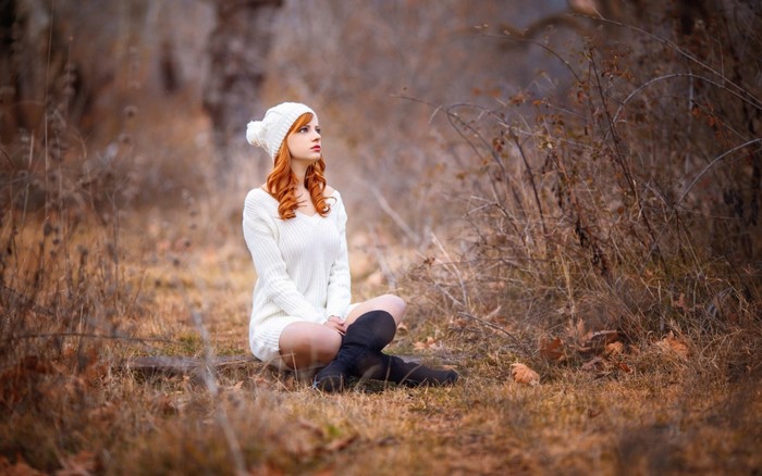 Redhead woman in white sweater and hat sitting in autumn forest