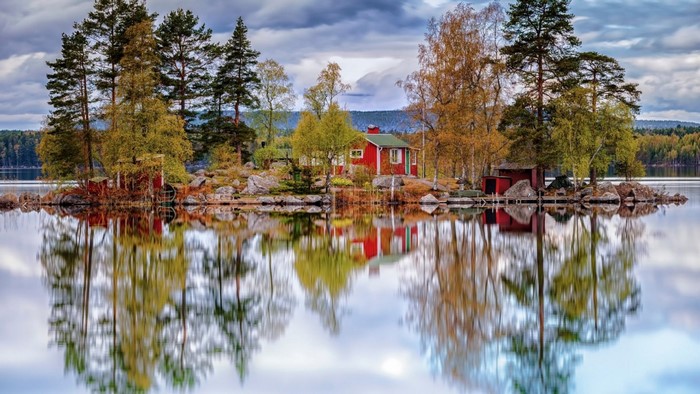 Red cabin on an island with autumn trees reflected in the lake