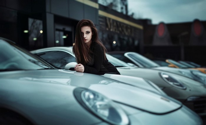 Woman in black dress leaning on a Porsche
