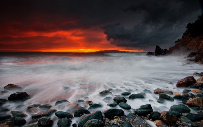 Dramatic sunset over a rocky shore with crashing waves