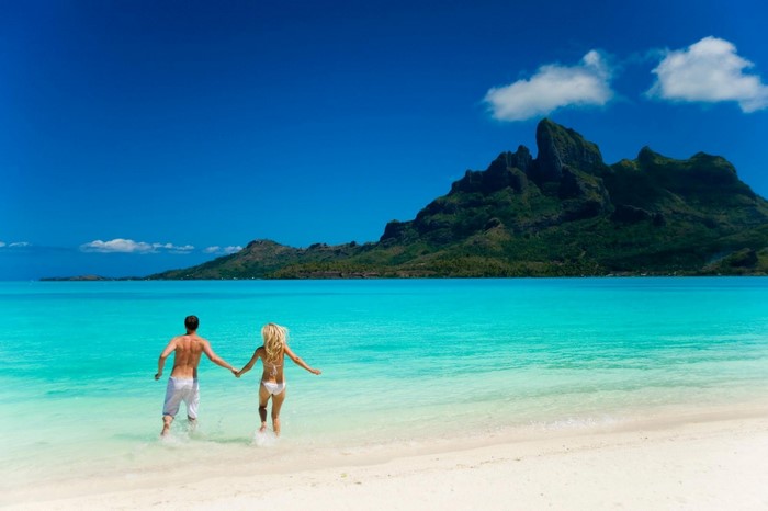 Couple running into the turquoise water of a tropical island lagoon