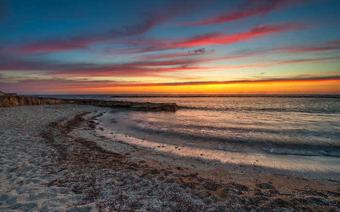 Sunset over a beach with colorful clouds and ocean waves